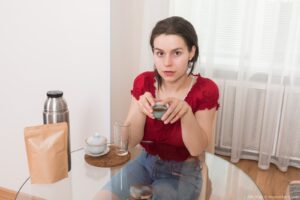 Petite busty brunette Ole Nina sips tea before disrobing and showing her big mound of pubic hair - OleNina_RedShirtDenimJeans_001